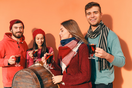 Smiling european men and women during party photoshoot. The guys posing as friends at studio fest with wineglasses with hot mulled wine on foreground.の写真素材