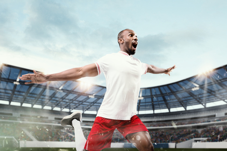 The football african player in motion on the field of stadium at day. The professional football, soccer player and human emotions concept. The win, winner, victory conceptの写真素材