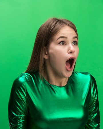 The surprised and astonished young woman screaming with open mouth isolated on green background. concept of shock face human emotionの写真素材