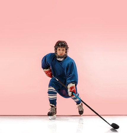 A hockey player in uniform with equipment over pink studio background. The athlete, child, sport, action conceptの写真素材
