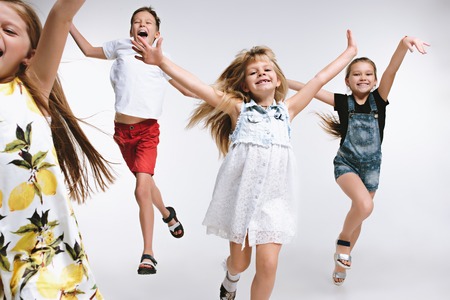 Group of fashion cute preschooler kids friends running together and looking at camera on a white studio background. The friendship, fashion, summer concept. Space for text.の写真素材