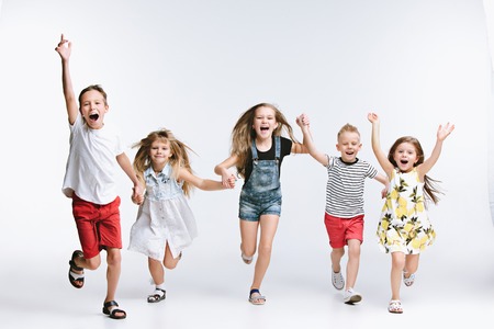 Group of fashion cute preschooler kids friends running together and looking at camera on a white studio background. The friendship, fashion, summer concept. Space for text.の写真素材