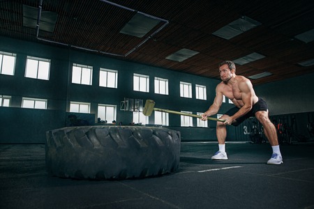Shirtless young fit man flipping heavy tire at gym. The exercise, fitness, sport, workout, athlete, power, training, bodybuilding conceptの写真素材
