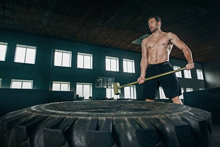 Shirtless young fit man flipping heavy tire at gym. The exercise, fitness, sport, workout, athlete, power, training, bodybuilding conceptの写真素材