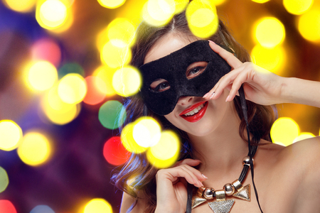 Beauty model woman wearing venetian masquerade carnival mask at party over holiday dark background with magic glow. Christmas and New Year celebration. Glamour lady with perfect make up and hairstyleの写真素材