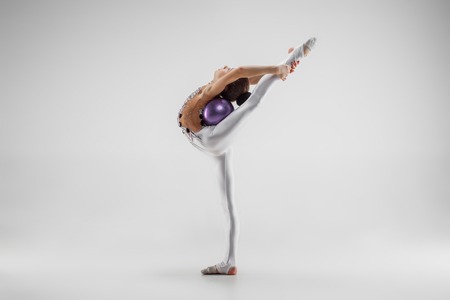 The teen female little girl doing gymnastics exercises with ball on a gray studio background. The gymnastic, stretch, fitness, lifestyle, training, sport conceptの写真素材