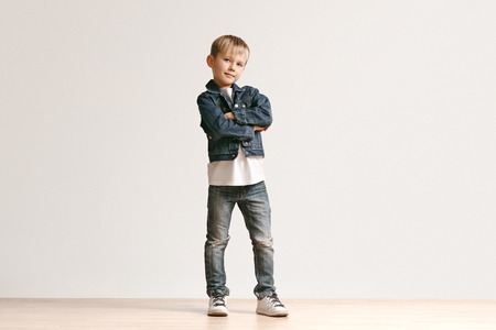 The portrait of cute little kid boy in stylish jeans clothes looking at camera against white studio wall. Kids fashion conceptの写真素材