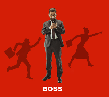 Handsome businessman with mobile phone. Serious business man standing isolated on red background. Boss conceptの写真素材