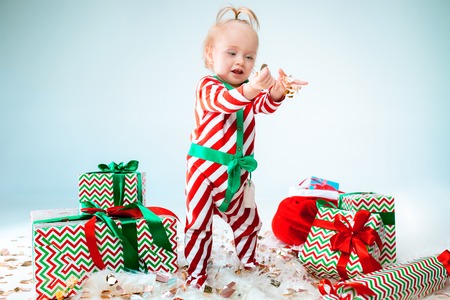 Cute baby girl 1 year old wearing santa hat posing over Christmas background. Standing on floor with Christmas ball. Holiday season.の写真素材
