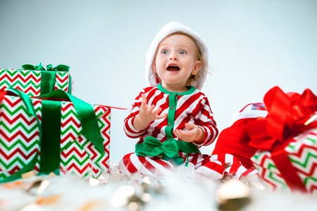 Cute baby girl 1 year old wearing santa hat posing over Christmas decorations with gifts. Sitting on floor with Christmas ball. Holiday season.の写真素材