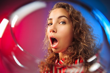The surprised young woman in party clothes posing with glass of wine.の写真素材