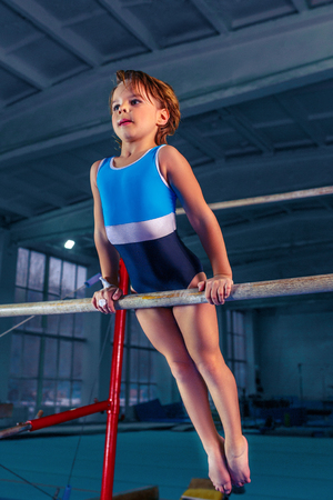 The beautiful little girl is engaged in sports gymnastics on a parallel bars at gym.の写真素材