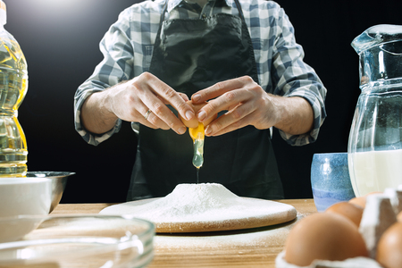 Professional male cook sprinkles dough with flour, prepares or bakes bread or pasta at kitchen tableの写真素材
