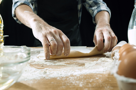 Professional male cook sprinkles dough with flour, prepares or bakes bread or pasta at kitchen tableの素材 [FY310113873635]