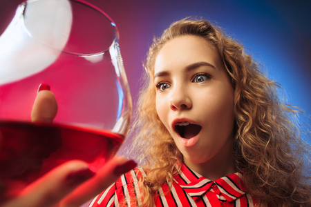 The surprised young woman in party clothes posing with glass of wine. Emotional female cute face. View from the glassの写真素材