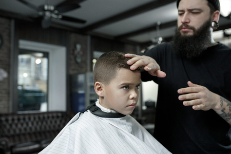 Children hairdresser cutting little boys hair. Contented cute preschooler boy getting the haircut.の写真素材