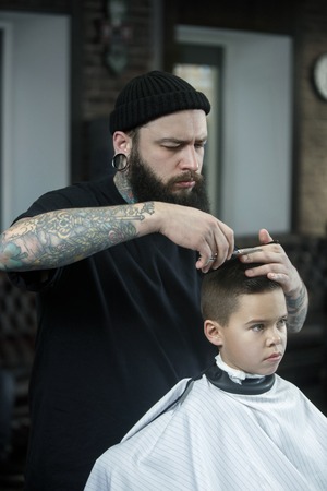 Children hairdresser cutting little boys hair. Contented cute preschooler boy getting the haircut.
