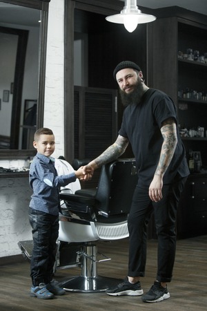 Children hairdresser and little boy against a dark background after haircut