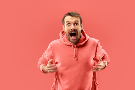 Wow. Attractive male half-length portrait on coral studio backgroud. Young emotional surprised bearded man standing with open mouth. Human emotions, facial expression concept. Trendy colorsの写真素材