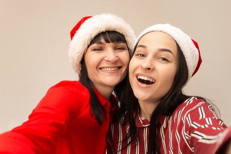 A portrait of a happy mother and daughter in Santa hat at studio on gray background. Human positive emotions and facial expressions conceptの写真素材