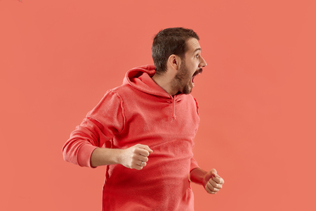 Screaming, hate, rage. Crying emotional angry man screaming on coral studio background. Emotional, young face. male half-length portrait. Human emotions, facial expression concept. Trendy colorsの写真素材