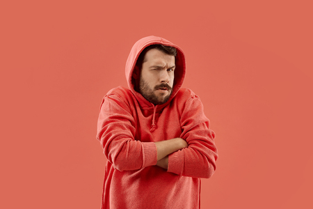 Suspicion. Doubt, mistrust, distrust concept. Doubtful man looking with disbelief expression . Young emotional man. Human emotions, facial expression concept. Studio. Isolated on trendy coralの写真素材