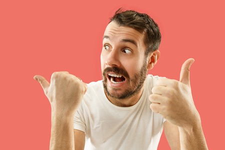 Wow. Attractive male half-length front portrait on coral studio backgroud. Young emotional surprised bearded man standing with open mouth. Human emotions, facial expression concept. Trendy colorsの写真素材