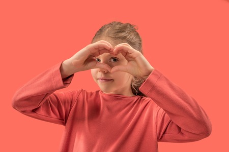 young girl forming a heart with her fingers over coral. Human emotions and facial expression over trendy colorの写真素材