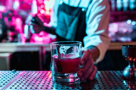 Expert barman is making cocktail at night club or bar. Glass of fiery cocktail on the bar counter...