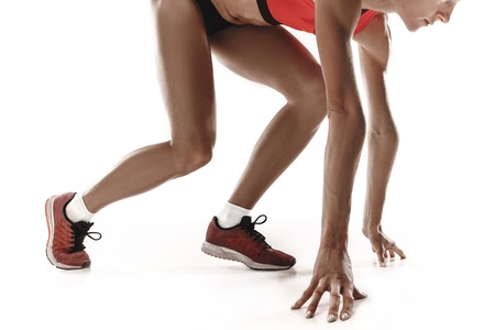 Portrait of young sporty woman at starting block of race isolated over white studio background. The...