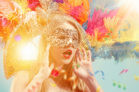 Beautiful young woman in carnival mask. Beauty model woman wearing masquerade mask at party over holiday background with magic glow. Christmas and New Year celebration. Glamour lady with perfect make up and hairstyleの写真素材
