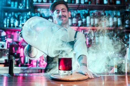 Expert barman is making cocktail at night club or bar. Glass of fiery cocktail on the bar counter against the background of bartenders hands with fire. Barman day conceptの写真素材