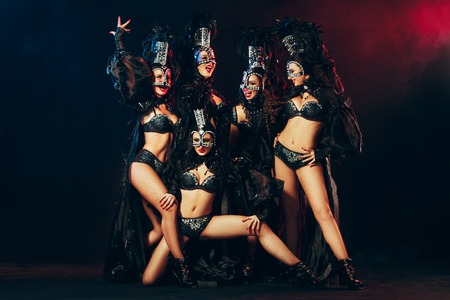 The group of young happy smiling beautiful female dancers with carnival dresses posing on black studioの写真素材