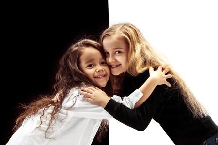 The portrait of two hugging embracing happy girls on a white and black studioの写真素材