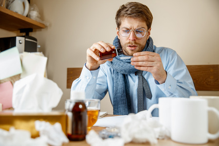Sick man with medicinal mixture working in office, businessman caught cold, seasonal flu.の写真素材