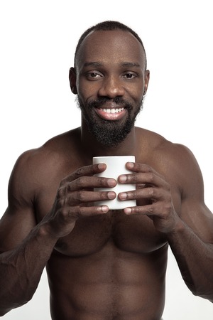 African man with white cup of tea or coffee, isolated on white studio background. Close up portrait in minimalism style of a young naked happy afro manの写真素材