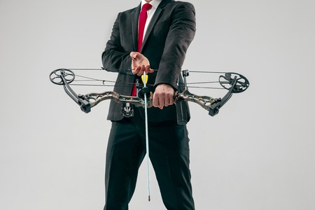 Businessman aiming at target with bow and arrow isolated on gray studioの写真素材