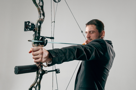 Businessman aiming at target with bow and arrow isolated on gray studioの写真素材