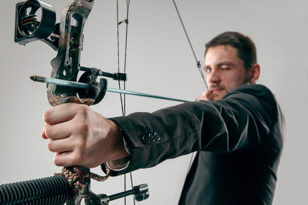 Businessman aiming at target with bow and arrow isolated on gray studioの写真素材