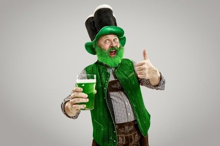 A smiling happy senior man in a leprechaun hat with green beer at studio.