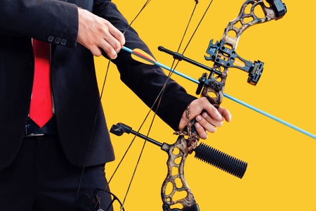Businessman aiming at target with bow and arrow, isolated on yellow studio