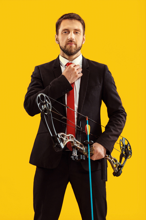 Businessman aiming at target with bow and arrow, isolated on yellow studioの写真素材