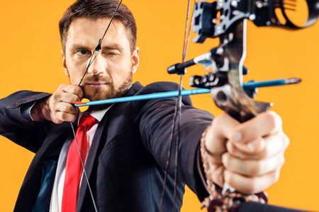 Businessman aiming at target with bow and arrow, isolated on yellow studioの写真素材