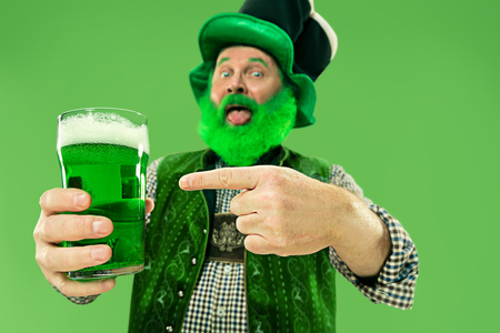 A smiling happy senior man in a leprechaun hat with green beer at studio. He celebrates St. Patricks Day. The celebration, festive, beer, holiday, alcohol, party conceptの写真素材