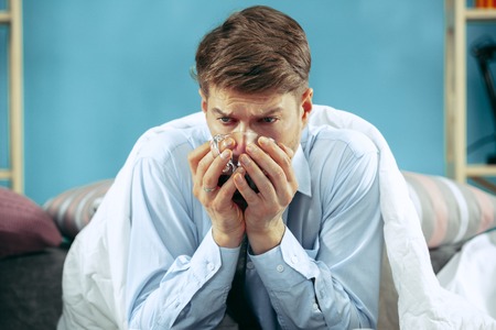 Bearded sick man with flue sitting on sofa at home and drinking tea. The winter, illness, influenza, pain concept. Relaxation at Home. Healthcare Concepts.の写真素材
