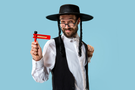 Portrait of a young orthodox Hasdim Jewish man with wooden Grager Ratchet at Jewish festival of Purim at studio. The purim, jewish, festival, holiday, celebration, judaism, pastry, tradition, cookie, religion concept.の写真素材