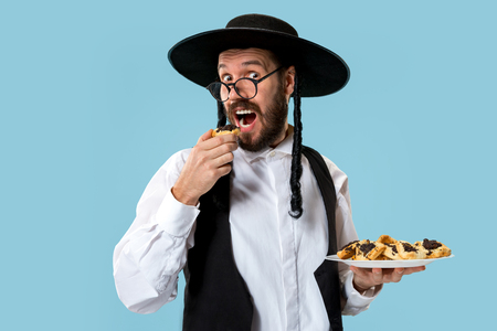 The young orthodox Jewish man with black hat with Hamantaschen cookies for Jewish festival of Purim at studio. The purim, jewish, festival, holiday, celebration, judaism, pastry, tradition, cookie, religion conceptの写真素材