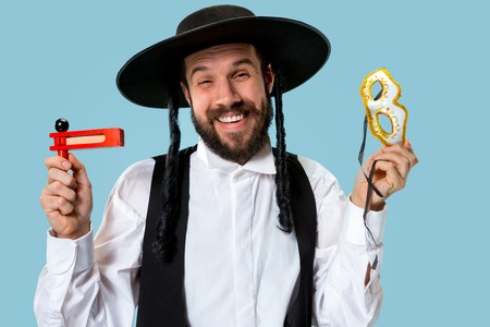 Portrait of a young orthodox Hasdim Jewish man with wooden Grager Ratchet at Jewish festival of Purim at studio. The purim, jewish, festival, holiday, celebration, judaism, pastry, tradition, cookie, religion concept.の写真素材
