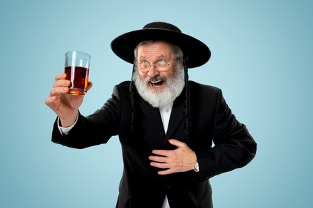 Portrait of old senior orthodox Hasdim Jewish man with kosher wine at Jewish festival of Purim at studio. The purim, jewish, festival, holiday, celebration, judaism, pastry, tradition, cookie, religion concept.