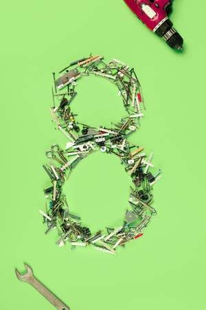 The conceptual composition from set of nails, screws and tools about Eight march womans day holiday on a green background. The number 8 in decor. Top view. The women in male occupationsの写真素材